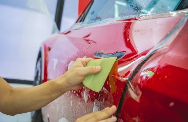 Yeni kırmızı arabaya koruyucu film yükleme işlemi