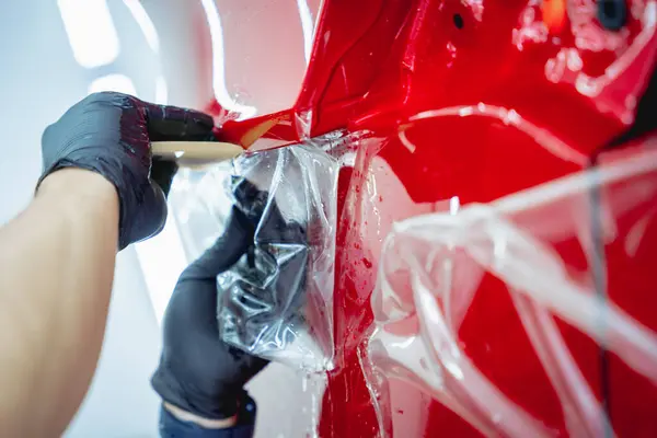 Araba servisindeki işçiler koruyucu film uygulamadan önce arabaya su sıkarlar.