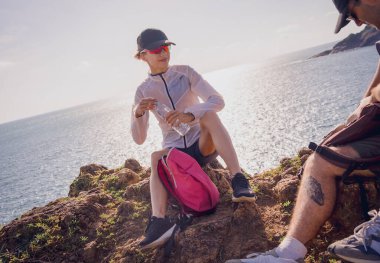 Mutlu genç çift okyanus kıyısındaki dağların tepesine tırmandıktan sonra rahatlıyor..