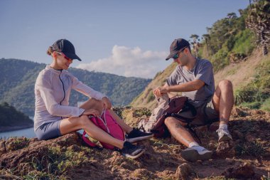 Mutlu genç çift okyanus kıyısındaki dağların tepesine tırmandıktan sonra rahatlıyor..