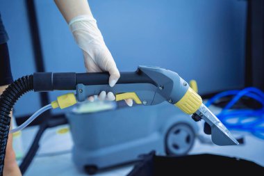 Arabayı temizleyen genç bir kadın elektrikli süpürgeyle temizlik yapıyor..