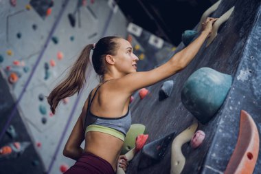 Güçlü bir dişi tırmanıcı renkli tutacakları ve ipleriyle yapay bir duvara tırmanır.