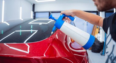 Araba servisindeki işçiler koruyucu film uygulamadan önce arabaya su sıkarlar.