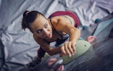 Güçlü bir dişi tırmanıcı renkli tutacakları ve ipleriyle yapay bir duvara tırmanır.