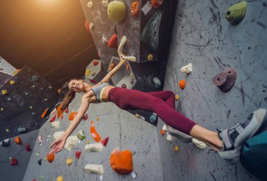 Güçlü bir dişi tırmanıcı renkli tutacakları ve ipleriyle yapay bir duvara tırmanır.