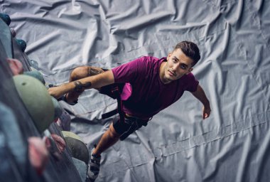 Güçlü bir erkek tırmanıcı renkli tutacakları ve ipleriyle yapay bir duvara tırmanır.