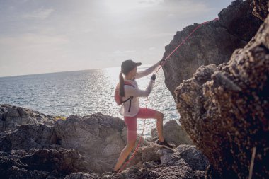 İpi olan genç bir kadın okyanusun yanındaki dağların tepesine tırmanır..