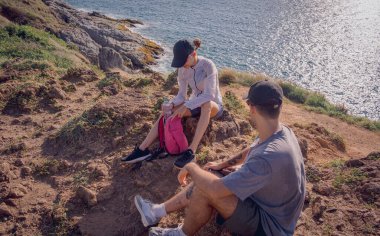 Mutlu genç çift okyanus kıyısındaki dağların tepesine tırmandıktan sonra rahatlıyor..