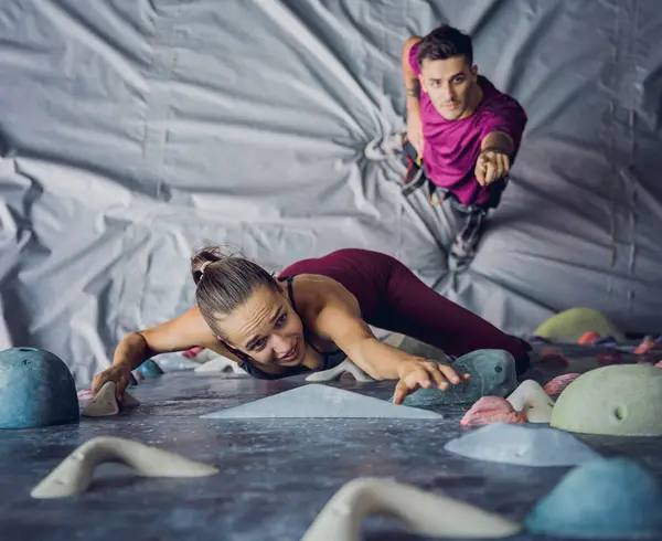 A strong couple of climbers climb an artificial wall with colorful grips and ropes