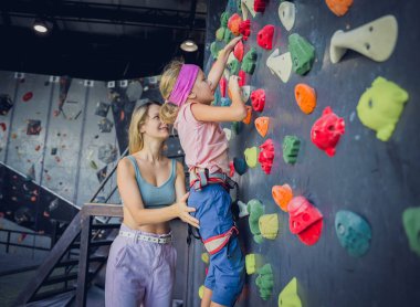 Güçlü bir bebek tırmanıcı renkli tutacakları ve ipleriyle yapay bir duvara tırmanır.