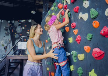 Güçlü bir bebek tırmanıcı renkli tutacakları ve ipleriyle yapay bir duvara tırmanır.