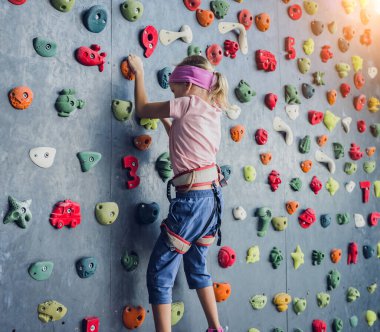 Güçlü bir bebek tırmanıcı renkli tutacakları ve ipleriyle yapay bir duvara tırmanır.