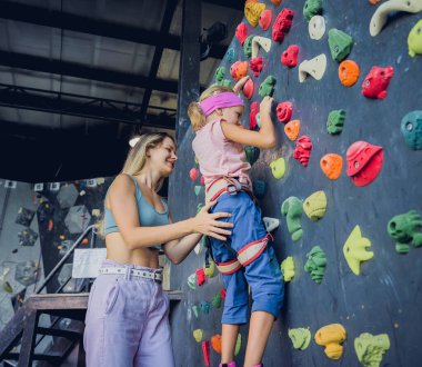 Güçlü bir bebek tırmanıcı renkli tutacakları ve ipleriyle yapay bir duvara tırmanır.