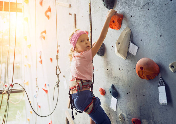 A strong baby climber climbs an artificial wall with colorful grips and ropes