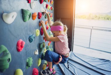 Güçlü bir bebek tırmanıcı renkli tutacakları ve ipleriyle yapay bir duvara tırmanır.