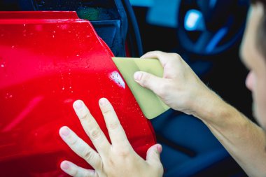 Yeni kırmızı arabaya koruyucu film yükleme işlemi