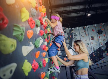Güçlü bir bebek tırmanıcı renkli tutacakları ve ipleriyle yapay bir duvara tırmanır.