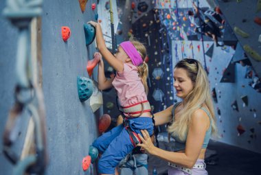 Güçlü bir bebek tırmanıcı renkli tutacakları ve ipleriyle yapay bir duvara tırmanır.