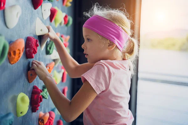 A strong baby climber climbs an artificial wall with colorful grips and ropes