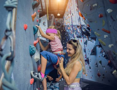 Güçlü bir bebek tırmanıcı renkli tutacakları ve ipleriyle yapay bir duvara tırmanır.