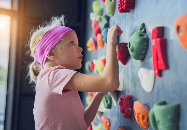 A strong baby climber climbs an artificial wall with colorful grips and ropes