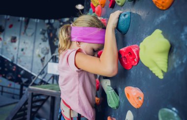 Güçlü bir bebek tırmanıcı renkli tutacakları ve ipleriyle yapay bir duvara tırmanır.