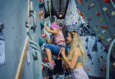 Güçlü bir bebek tırmanıcı renkli tutacakları ve ipleriyle yapay bir duvara tırmanır.