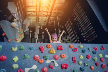 Güçlü bir bebek tırmanıcı renkli tutacakları ve ipleriyle yapay bir duvara tırmanır.