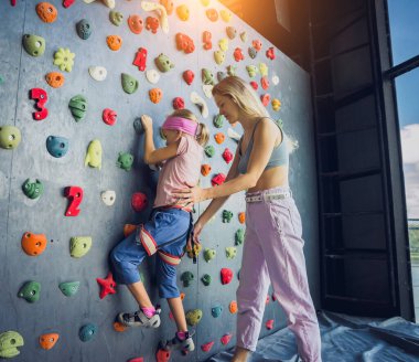 Güçlü bir bebek tırmanıcı renkli tutacakları ve ipleriyle yapay bir duvara tırmanır.