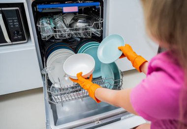 Genç kadın bulaşık makinesinden bulaşıkları çıkarıyor..