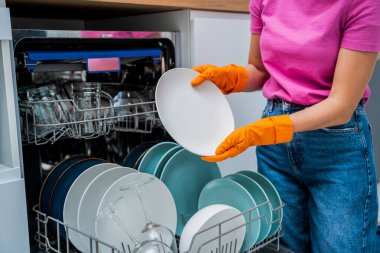 Genç kadın bulaşık makinesinden bulaşıkları çıkarıyor..