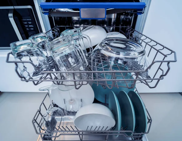 The white kitchen and opened dishwasher with clean dishes.