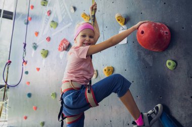 Güçlü bir bebek tırmanıcı renkli tutacakları ve ipleriyle yapay bir duvara tırmanır.