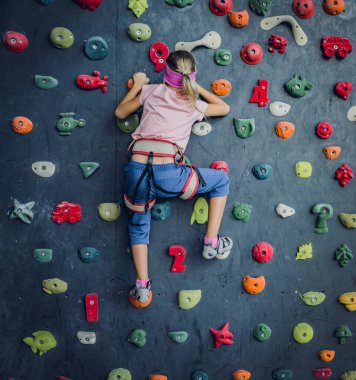 Güçlü bir bebek tırmanıcı renkli tutacakları ve ipleriyle yapay bir duvara tırmanır.