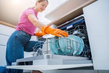 Genç kadın bulaşık makinesinden bulaşıkları çıkarıyor..