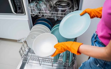 Genç kadın bulaşık makinesinden bulaşıkları çıkarıyor..