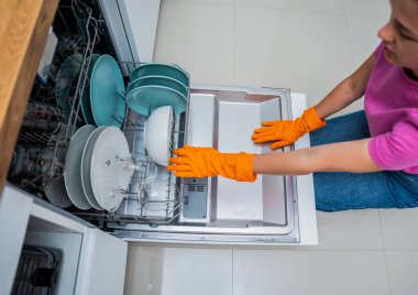 Genç kadın bulaşık makinesinden bulaşıkları çıkarıyor..