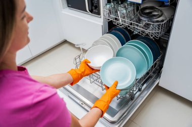 Genç kadın bulaşık makinesinden bulaşıkları çıkarıyor..