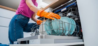 Genç kadın bulaşık makinesinden bulaşıkları çıkarıyor..