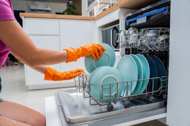 Genç kadın bulaşık makinesinden bulaşıkları çıkarıyor..