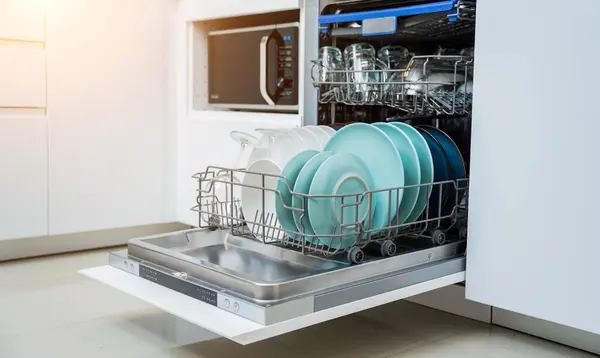 The white kitchen and opened dishwasher with clean dishes.