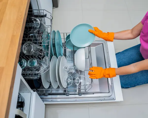 Genç kadın bulaşık makinesinden bulaşıkları çıkarıyor..