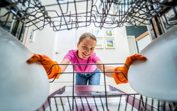 Genç kadın bulaşık makinesinden bulaşıkları çıkarıyor..