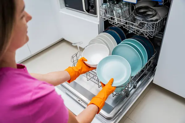 Genç kadın bulaşık makinesinden bulaşıkları çıkarıyor..