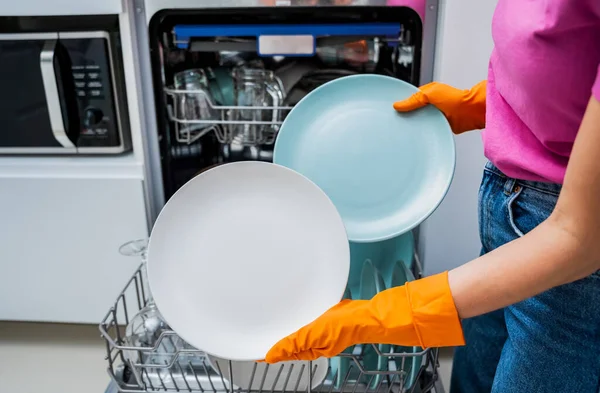 Young woman takes dishes out of the dishwasher machine.