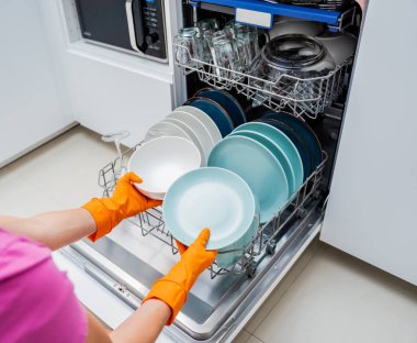 Genç kadın bulaşık makinesinden bulaşıkları çıkarıyor..