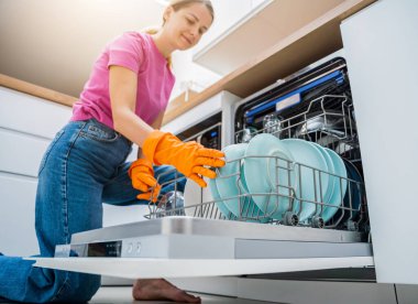 Genç kadın bulaşık makinesinden bulaşıkları çıkarıyor..