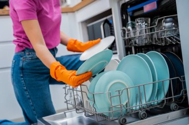 Genç kadın bulaşık makinesinden bulaşıkları çıkarıyor..