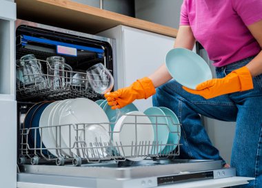 Genç kadın bulaşık makinesinden bulaşıkları çıkarıyor..