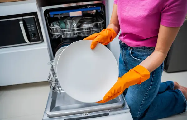 Genç kadın bulaşık makinesinden bulaşıkları çıkarıyor..